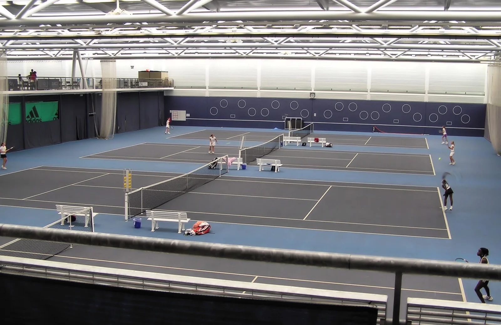 Blick über mehrere Hallentennisplätze mit blauem Belag in einer hellen Tennishalle